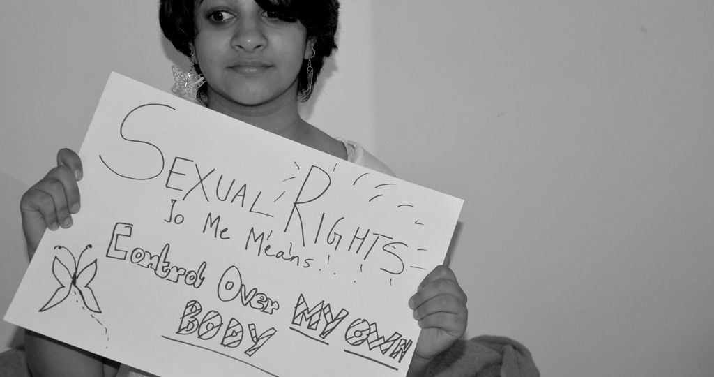 A person with short dark hair and silver earrings holds a sign that says "Sexual Rights To Me Means Control Over My Own Body". The photo is in black and white.
