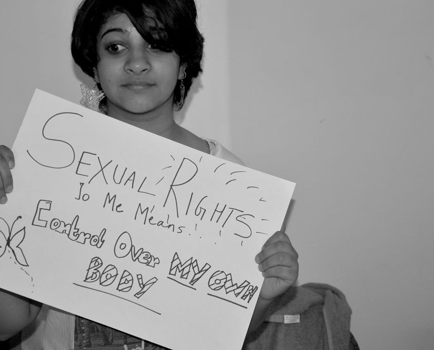 A person with short dark hair and silver earrings holds a sign that says "Sexual Rights To Me Means Control Over My Own Body". The photo is in black and white.