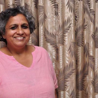 A photo of Anjali Gopalan, who has short black and gray hair and dark eyes. Anjali is smiling, wearing a light pink dupatta. Source: Naz Foundation