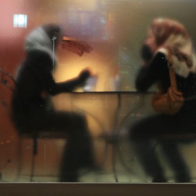 Two women wearing full black clothing and a headscarf sitting in a cafe. The photo is taken from other side of a glass door, such that they are blurred.