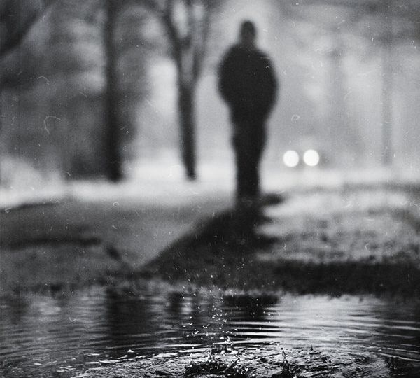 A drop of water falls on a water body. A silhoutted figure in black-and-white is seen in the background.