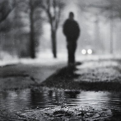 A drop of water falls on a water body. A silhoutted figure in black-and-white is seen in the background.
