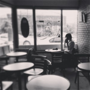 A black-and-white picture of a woman sitting in a cafeteria and sipping coffee