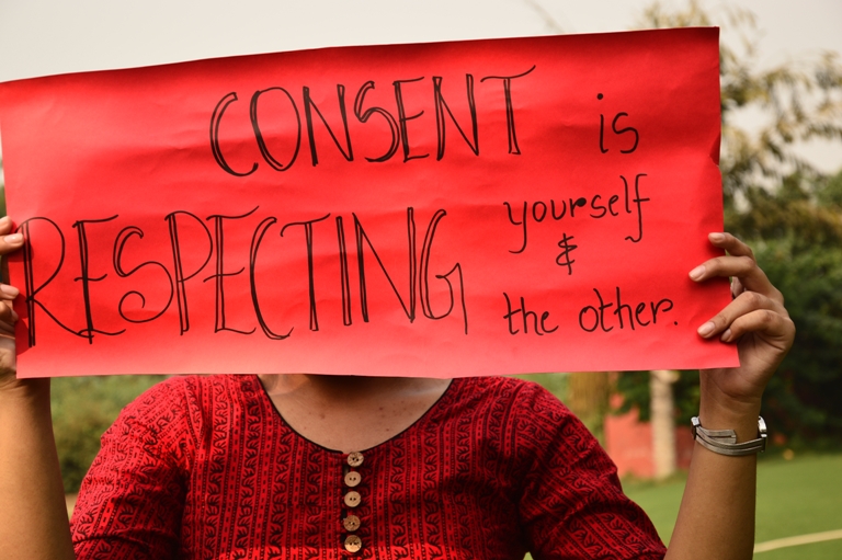Picture of a woman holding up a placard that says "Consent is respecting yourself and the other"