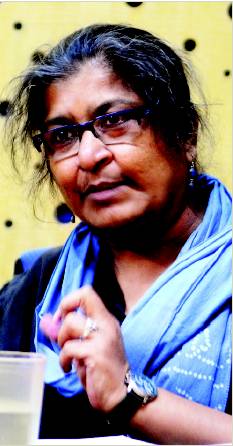 A picture of feminist scientist Chayanika Shah. Her hair is dark, with specks of grey. She has a blue scarf wrapped around her neck, and is wearing blue earrings.