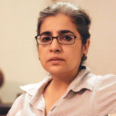 A picture of Pakistani feminist filmmaker Sabiha Sumar. Her dark hair has specks of gray in it, and she is wearing thick-rimmed glasses and a checked t shirt.