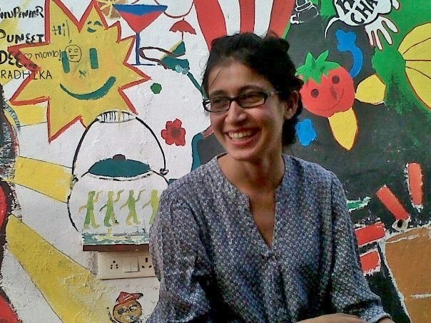 Photo of bodypositive activist Ekta Oza. She is wearing dark-rimmed glasses, a blue patterned kurta and her hair is tied back. She is looking to her left and laughing.