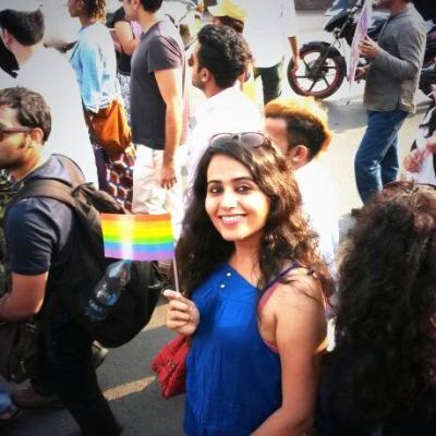 Photo of a woman in a pride parade, holding up a small queer pride flag