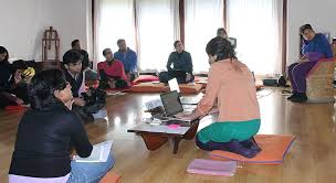 Picture of an ongoing workshop, where a woman sits in the middle with her laptop and there are people in the room sitting at various intervals around the woman and is listening to her talk.