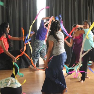 A group of women circling each other and dancing while waving colourful streamers.