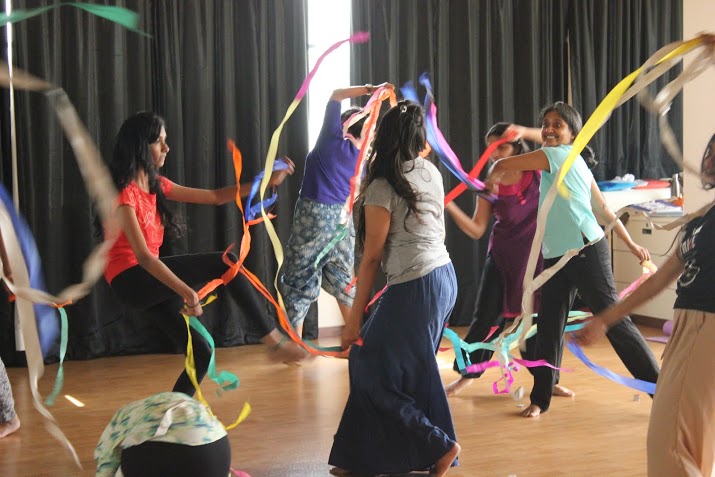 A group of women circling each other and dancing while waving colourful streamers.