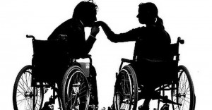 Silhouettes of a man and a woman sitting in two respective wheelchairs. The man is kissing the woman's hand