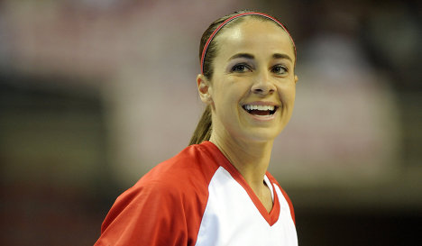 A picture of sports personality Becky Hammon. Her hair is tied back in a tight pnytail and she wears a red and white jersey. There is a smile on her face.