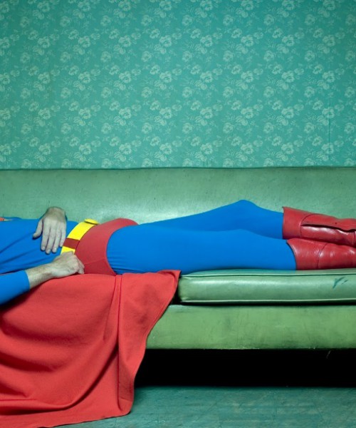 picture of man dressed as superman lying down on a sofa, against a green background