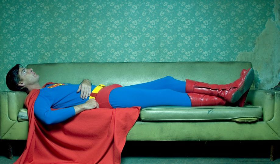 picture of man dressed as superman lying down on a sofa, against a green background