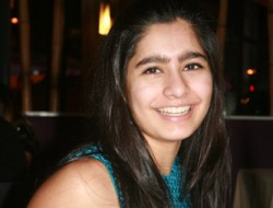 Photo of a woman who has long hair and is smiling into the camera. She is wearing a blue top.