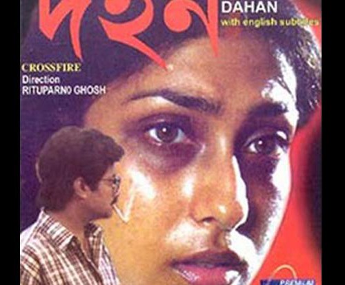 Poster for the Bengali film, 'Dahan', showing a woman's face enlarged and facing the camera, and the smaller figure of a man dressed in a chequered shirt looking at her