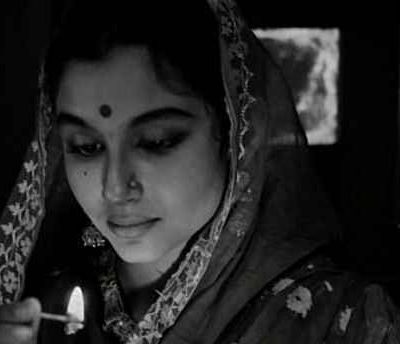 A still from the film "Apur Sansar" showing a woman who's looking downwards. She's wearing a saree and her aanchal is draped around her head.