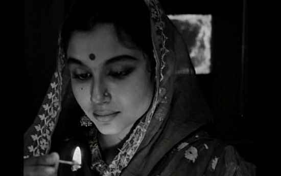 A still from the film "Apur Sansar" showing a woman who's looking downwards. She's wearing a saree and her aanchal is draped around her head.