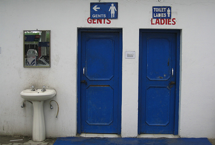 Two blue doors against a white wall, one having 'gents' and the othe rhaving 'ladies' written over it. beside them, there is a white sink.