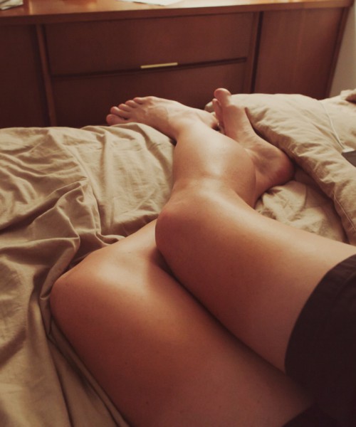 Photo showing a woman's legs as she lies on her bed over a light brown quilt, wearing black shorts.