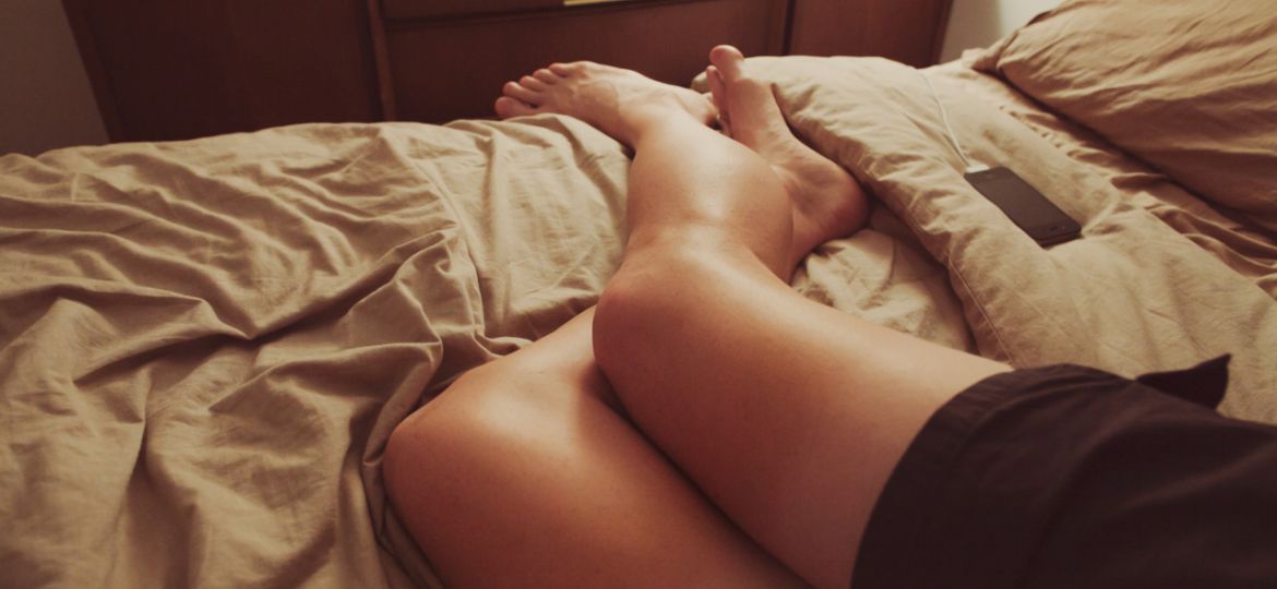 Photo showing a woman's legs as she lies on her bed over a light brown quilt, wearing black shorts.