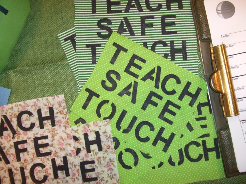 A series of pink and green placards that read 'Teach Safe Touch'