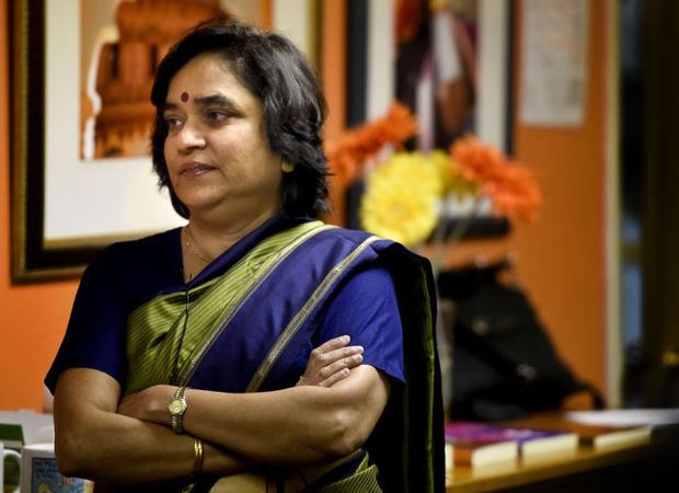 Ruth Vanita standing with her arms crossed. She is wearing a blue saree, a red bindi, watch on one hand, and golden bangle on another.