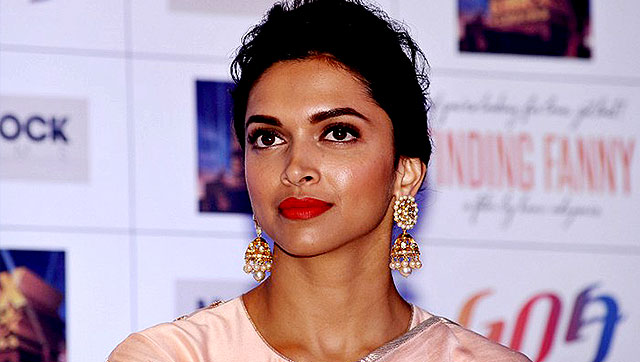 Headshot of actress Deepika Padukone. Her hair is tied back in a bun, and she is wearing gold earrings and a pastel pink salwar.