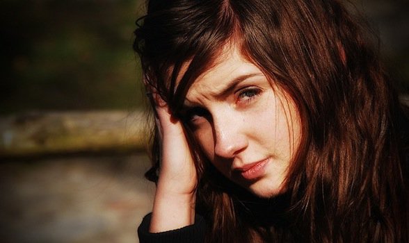 Headshot of a girl looking straight into the camera, one of her hands leaning against her head