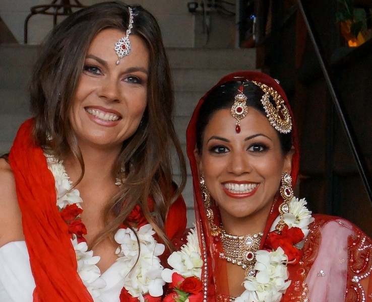 Photo of a lesbian couple, one of them dressed in Indian bridal clothes and the other dressed in Western bridal clothes
