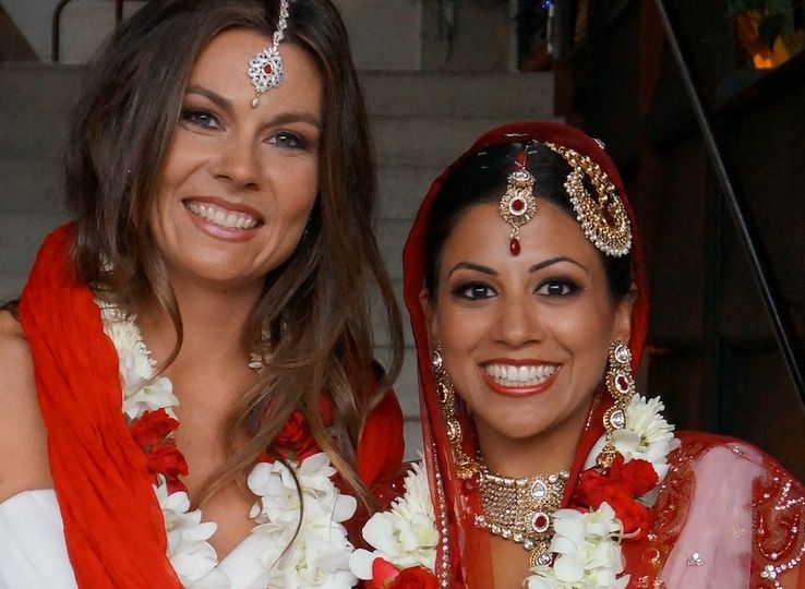 Photo of a lesbian couple, one of them dressed in Indian bridal clothes and the other dressed in Western bridal clothes