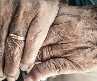 A pair of hands with wrinkles on them holding each other. One of the hands is wearing a gold band on their ring finger
