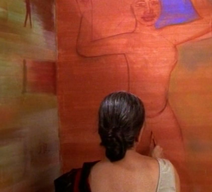 A woman in a black saree and white blouse faces a red wall, so that only her back is visible