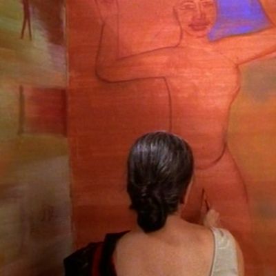 A woman in a black saree and white blouse faces a red wall, so that only her back is visible