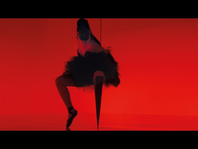 Against a red backdrop, the silhoutte of a dancing woman wearing a flare skirt