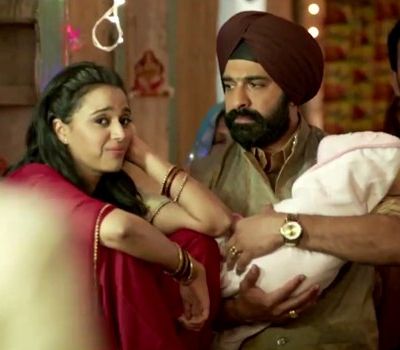 Still from film 'Tanu Weds Manu Returns'. A woman and a man in a wedding. The man holds a baby wrapped in a white cloth in his arms. The woman wears a red Indian suit, red bangles, and has open hair. The man wears a red turban and golden kurta.