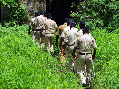 Some ten policemen in uniforms walking through a jungle in a queue.