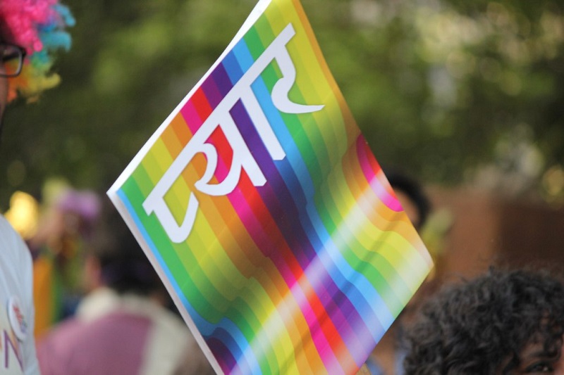 A placard reading "pyar" (love) in Hindi in white lettering on a rainbow-coloured background.