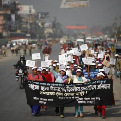 Nepalese women on a protest march. They are carrying a poster that reads in Hindi, "Women Against Violence Day". They are wearing white caps, and holding placards.