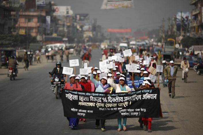 Nepalese women on a protest march. They are carrying a poster that reads in Hindi, "Women Against Violence Day". They are wearing white caps, and holding placards.