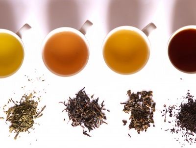 Four cups of different flavoured teas kept in a row horizontally. Next to each is kept corresponding dry tea leaves.
