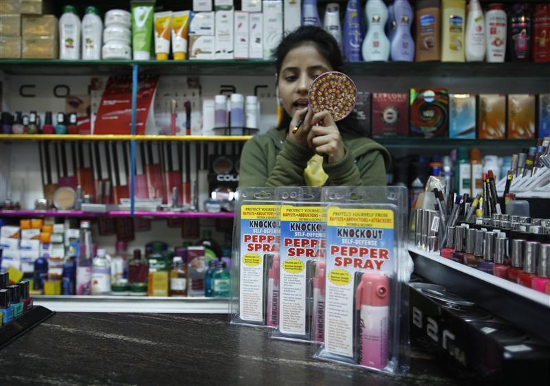 A salesgirl applies lipstick inside a shop with bottles of pepper spray displayed for sale in New Delhi