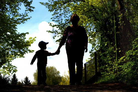 Silhouette of a woman with a little boy walking in a park, hand in hand.