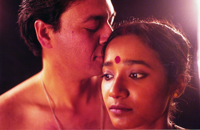 Still from film "The Lovedance" (2000). A bare-chested man smelling a woman's hair from behind. She wears a red bindi on her forehead.