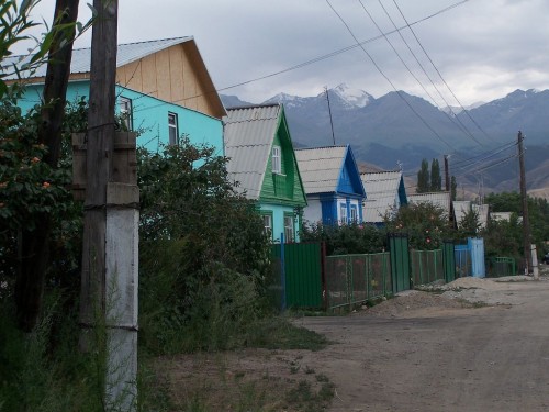 Street with tin roof houses in a hilly area. Snow-capped mountains can be seen behind.