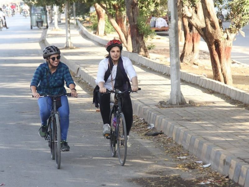 Two women cycling together on a derted street lined with trees