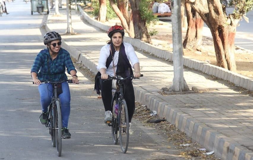 Two women cycling together on a derted street lined with trees