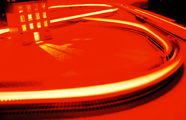 In bright orange light, a toy train races around a track that surrounds a toy sized building