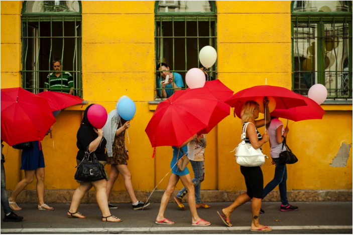 A group of women walking holding red umbrellas that cover their faces.